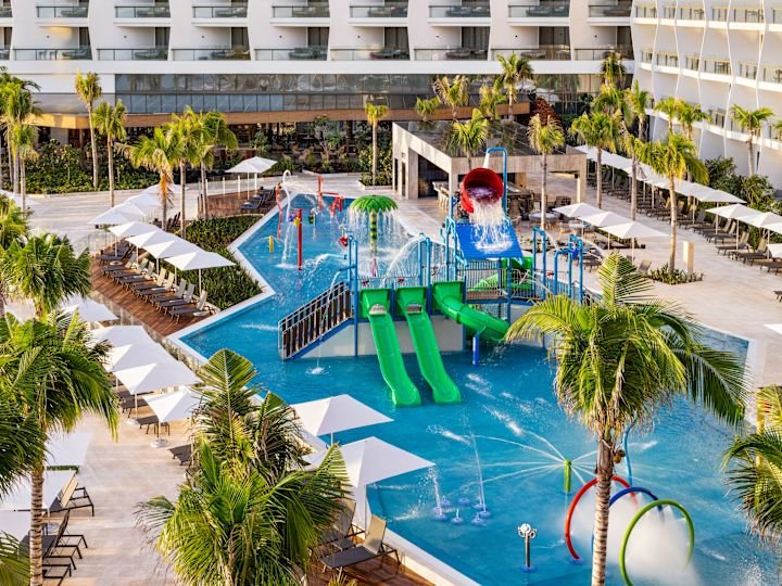 Green water slides and splash features beside a shallow pool at Hilton Cancún